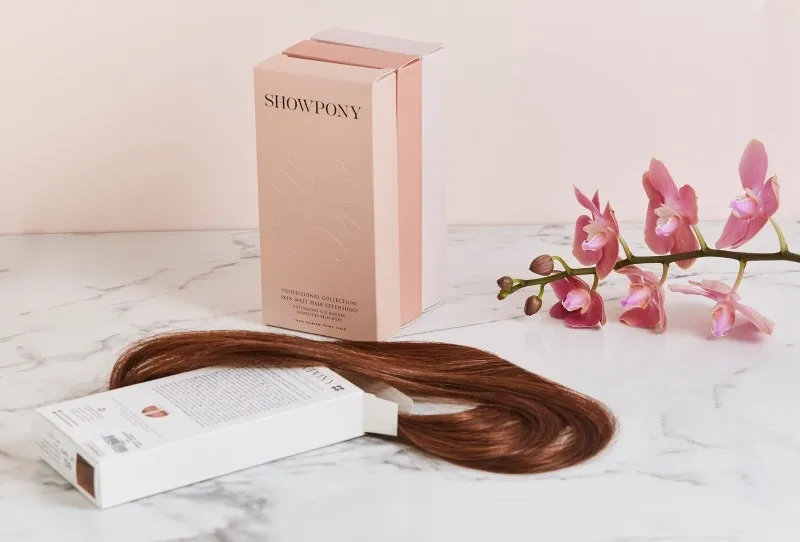 Showpony hair extensions box and a length of brunette extension hair on marble, with a pink orchid stem.